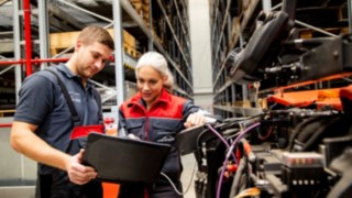 Doi tehnicieni de service Linde Material Handling se uită la un laptop lângă un stivuitor.