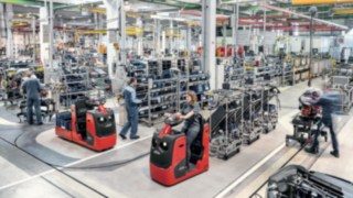 Echipamentele de tractare cu mai multe cărucioare cresc productivitatea aprovizionării cu componente. Echipament de tractare cu mai multe cărucioare, transportând componente către linia de producție.