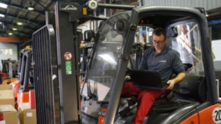Tehnicianul inspectează un stivuitor second hand Tehnician cu laptop care inspectează un stivuitor pentru recondiționare