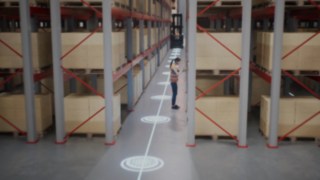 Animație care ilustrează un angajat în vestă de protecție în depozitul cu culoare înguste și zonele de siguranță pentru identificarea persoanelor