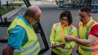 Trei persoane cu veste reflectorizante discută: Consultanță în materie de siguranță la sediul clientului. Trei persoane cu veste reflectorizante discută: Consultanță în materie de siguranță la sediul clientului.