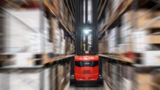 Două stivuitoare pentru culoare înguste de la Linde Material Handling, în acțiune într-o hală de depozitare.