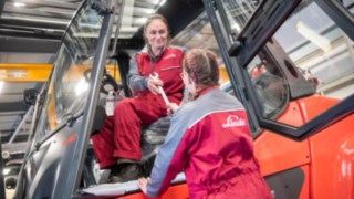 Angajații noștri joacă un rol central în politica noastră de dezvoltare sustenabilă. Un tehnician de service înmânează o unealtă unui alt tehnician de service care se află în stivuitor.