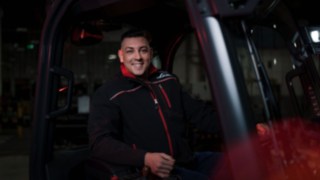 Un angajat Linde Material Handling stă într-un stivuitor industrial și zâmbește la cameră.