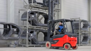 Linde Material Handling oferă soluții pentru principalele provocări intralogistice ale industriei auto. Operatorul stivuitorului Linde conduce până la un raft cu piese de caroserie