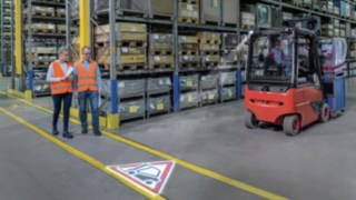 Linde TruckSpot transmite semnale în depozit Două persoane merg prin depozit și se intersectează cu un stivuitor