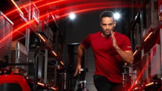 Un atlet aleargă într-un depozit, pe fundal se poate vedea stivuitorul cu catarg retractabil Linde MH Ri16.