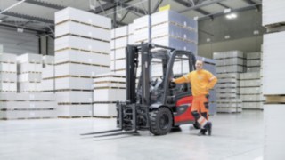 Un bărbat sprijinit de un stivuitor într-o hală de depozitare